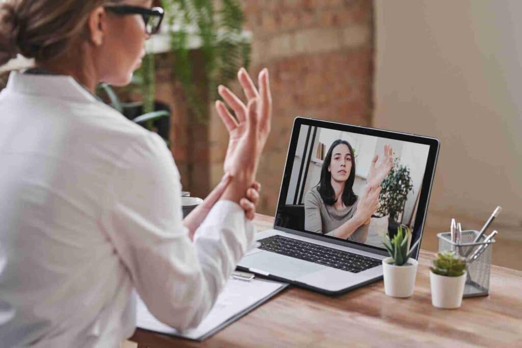 modern doctor wearing white coat sitting desk loft office having online appointment touching wrist joint camera scaled 1